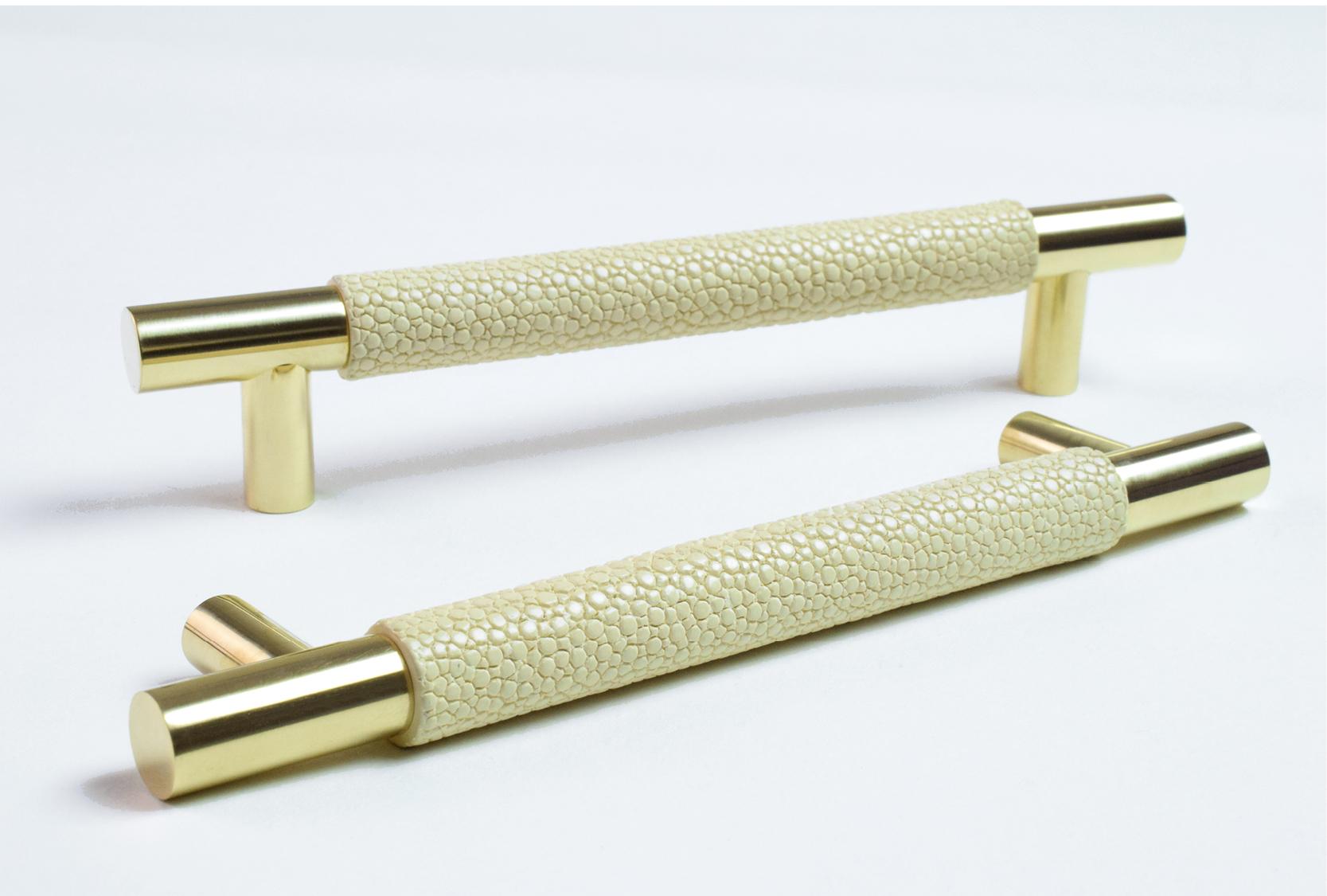 Image displays two custom shagreen cabinet pulls. One of the cabinet pulls are positioned on the side. The shagreen grip is in a custom cream colour. The pull ends and legs are finished in polished brass.
