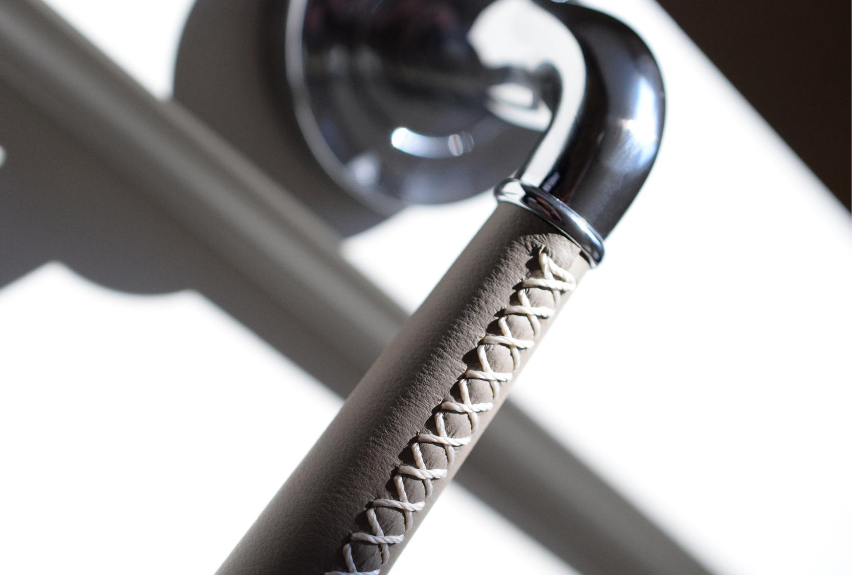 Grip of a Goose neck door lever with custom grey leather and cross stitch with natural thread.