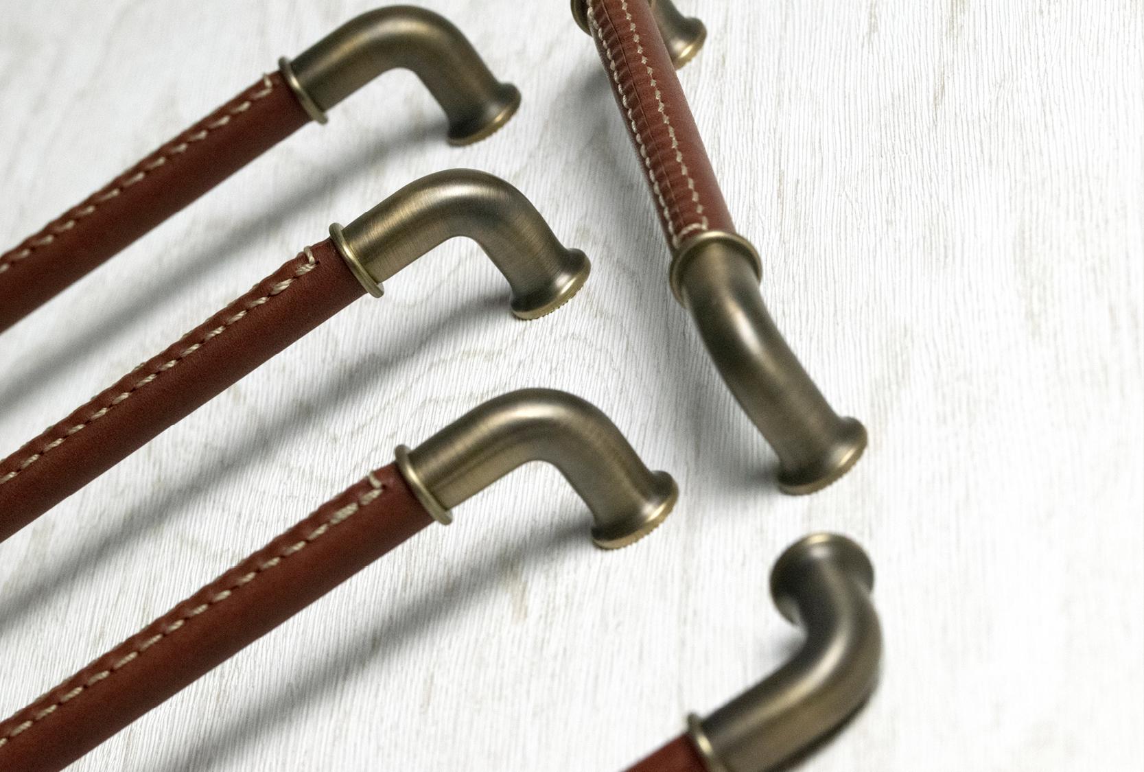 Image displays five custom length pipe recess leather Bonneville pull handles. Grip of the pull is finished in chestnut leather. The end caps and legs are finished in fine antique.