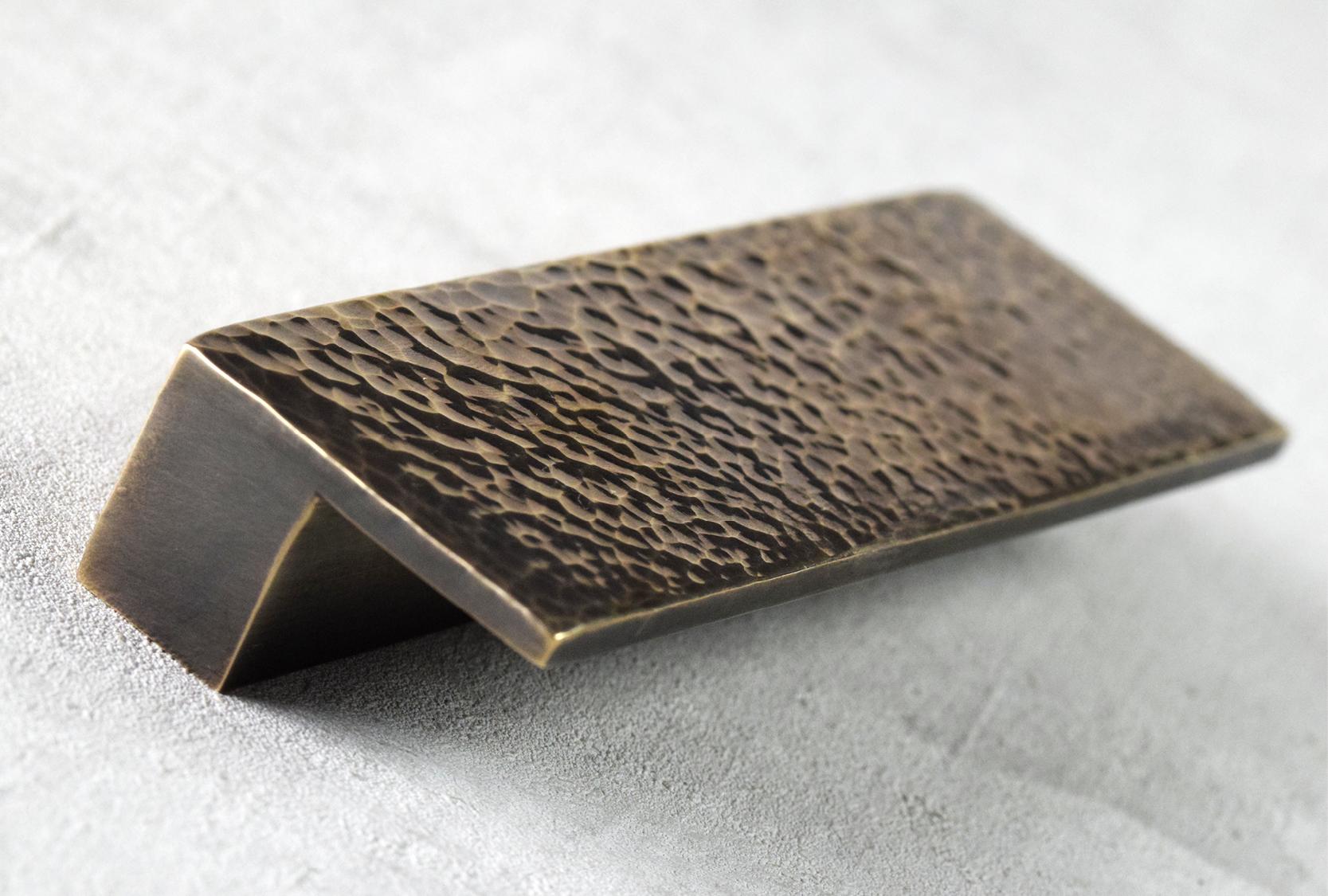 Image of a hand hammered ledge cabinet pull. Shown in burnished brass metal to really bring out the detail.