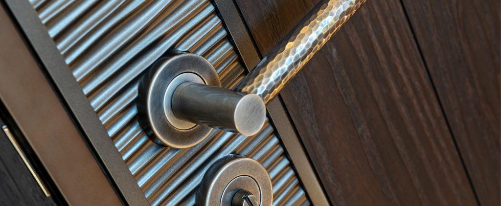 A hand hammered brass door lever on a decorative door. The door lever, by Turnstyle Designs, is a beautiful barrel shaped grip in Burnished Brass finish. Below the rose sits a release for the turn key on the other side.
