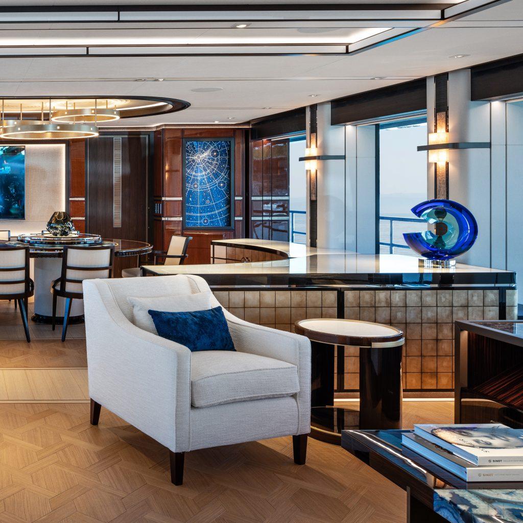The main salon on motor yacht Lusine, created by Heesen yachts. Decorated with mixture of light furniture, soft furnishings and dark veneer wood. Dark blue cushions and decor has been added for flashes of colour.