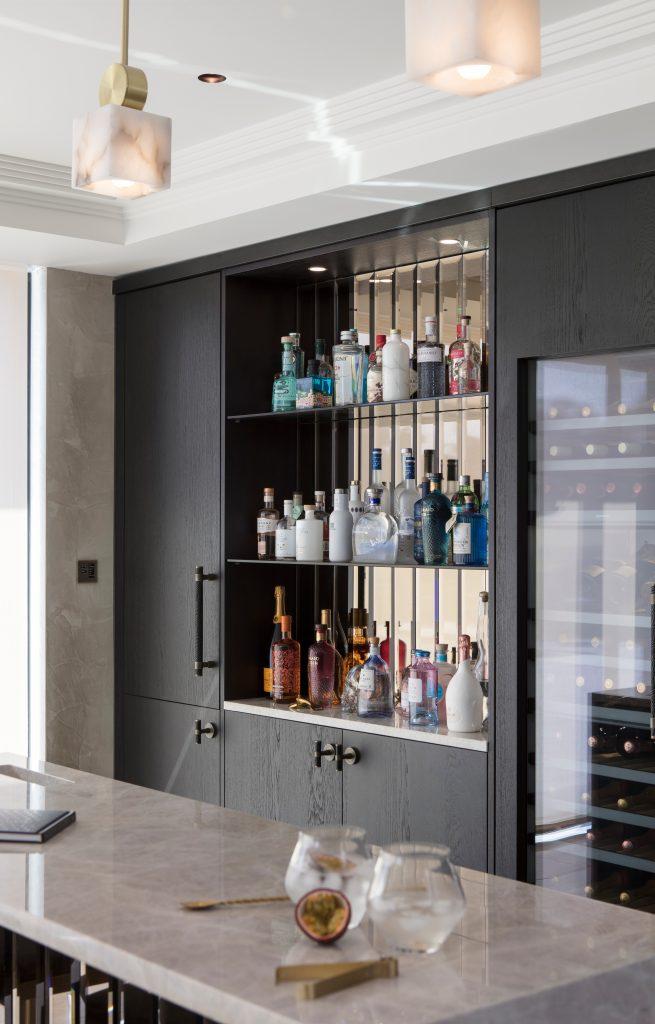 A luxury home bar in large kitchen extension. Using dark oak would and decorative handles, this unique styles entertaining area hosts a range of fine looking spirits and large wine cooler.