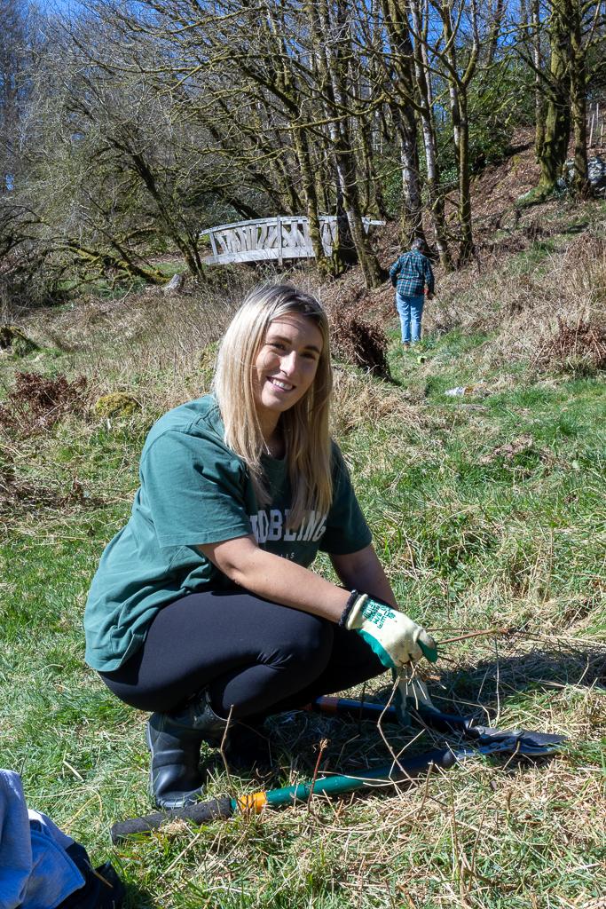 A young women with blonde hair helps clear a long gully of debris at Ashcombe Gardens, Simonsbath, Exmoor. This volunteer project with Exmoor National Park has a group f local volunteers help manage and maintain the local area.