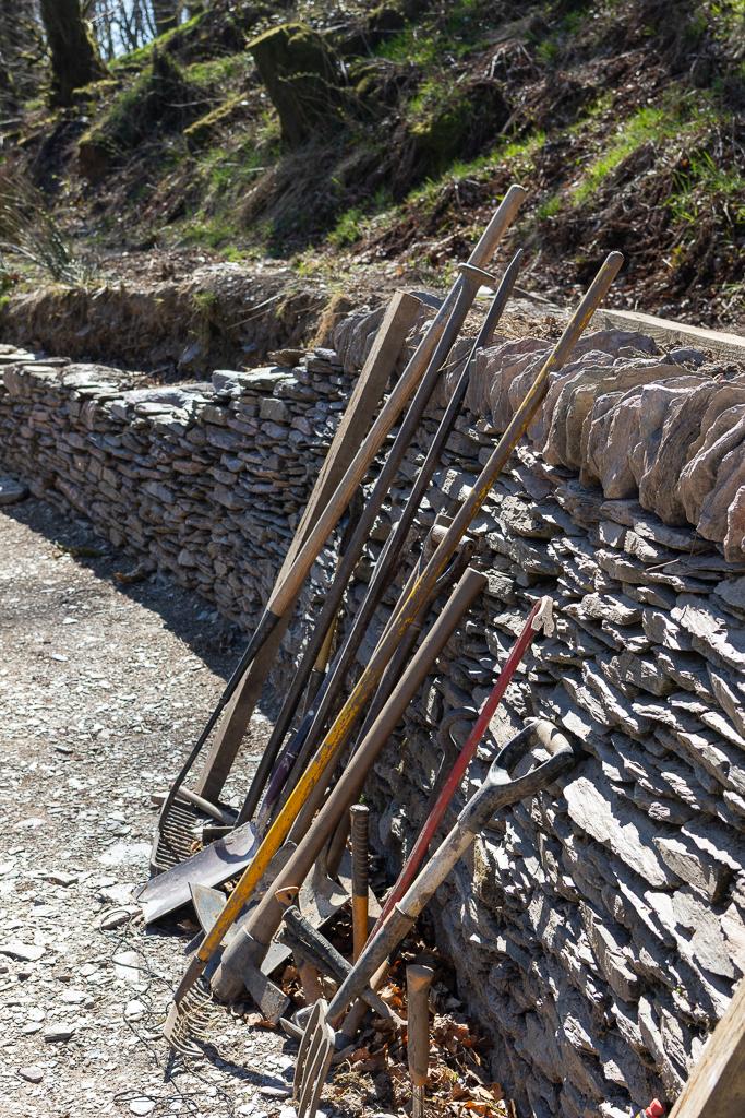 A selection of tools, rakes, spades and hooks lay up against a hand built Devon stone wall. This is part of the wild gardens project in Ashcombe Gardens in , Exmoor.